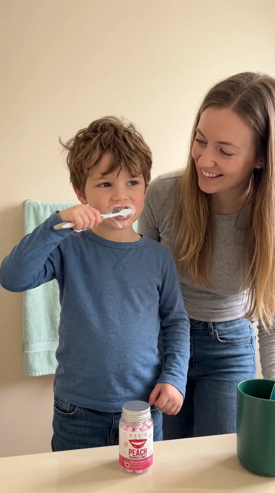 A boy brushes his teeth at the sink while his mom watches